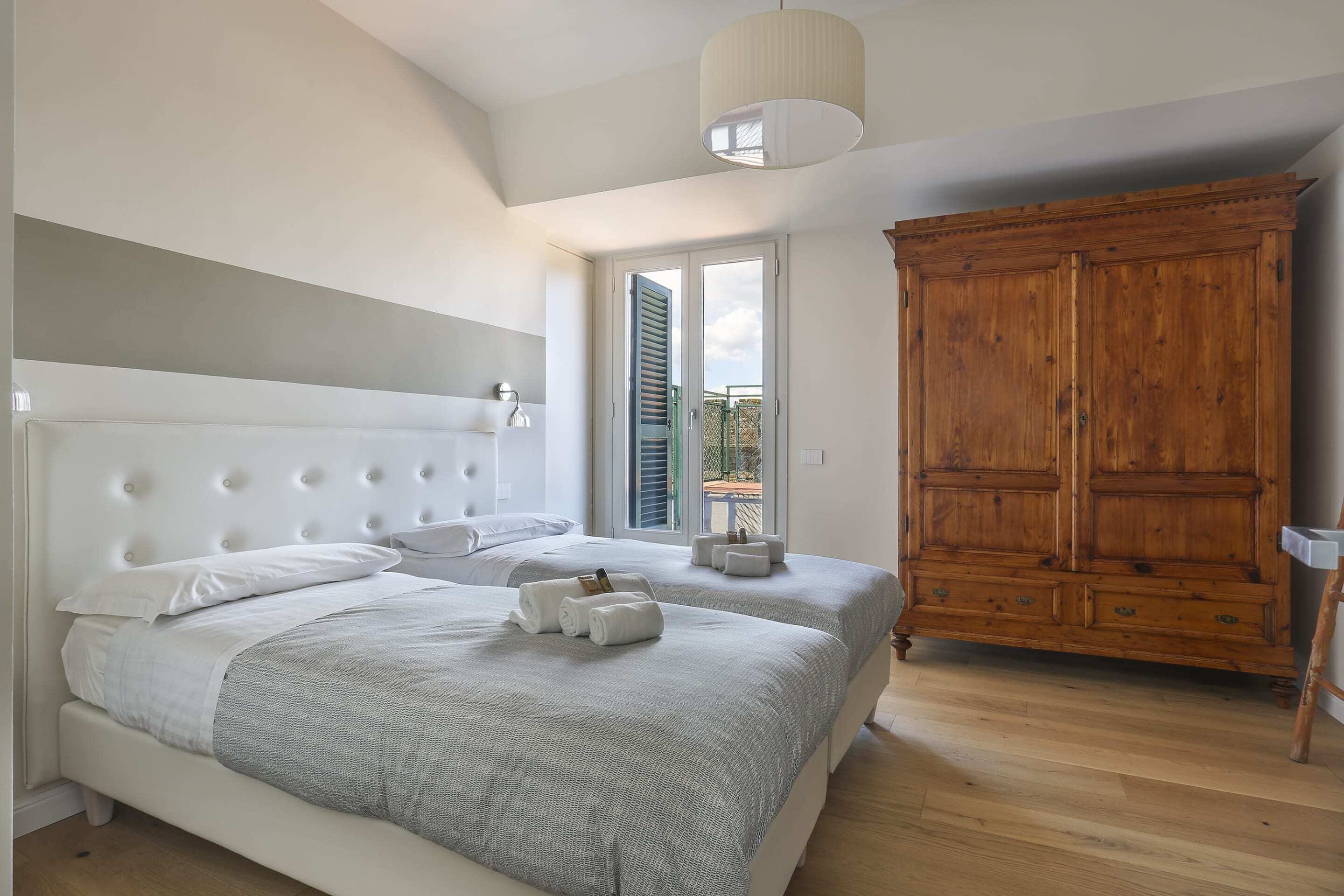 Une chambre avec deux lits, une armoire en bois et une grande fenêtre avec des volets.