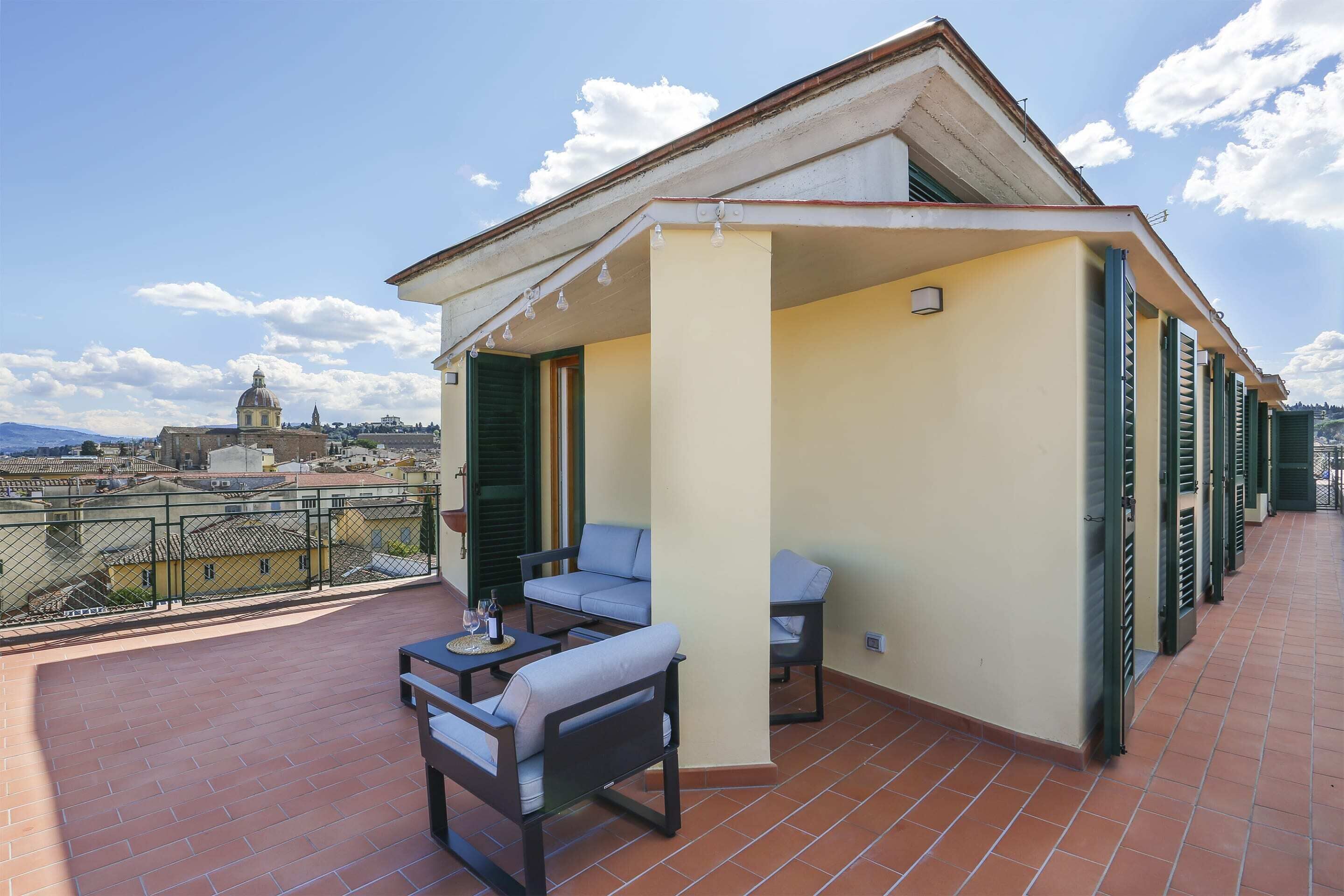 A balcony with a table and chairs, a view of a dome and buildings in the background, and a tiled floor.