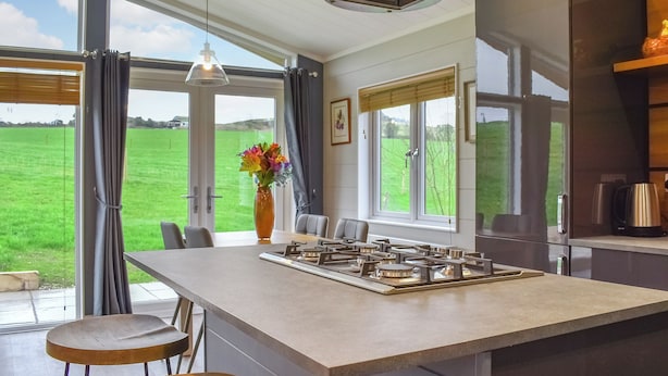 A modern kitchen with a large island, a gas stove, and a view of a green field through large windows. - Whitey Top Country Lodge (Pentridge)