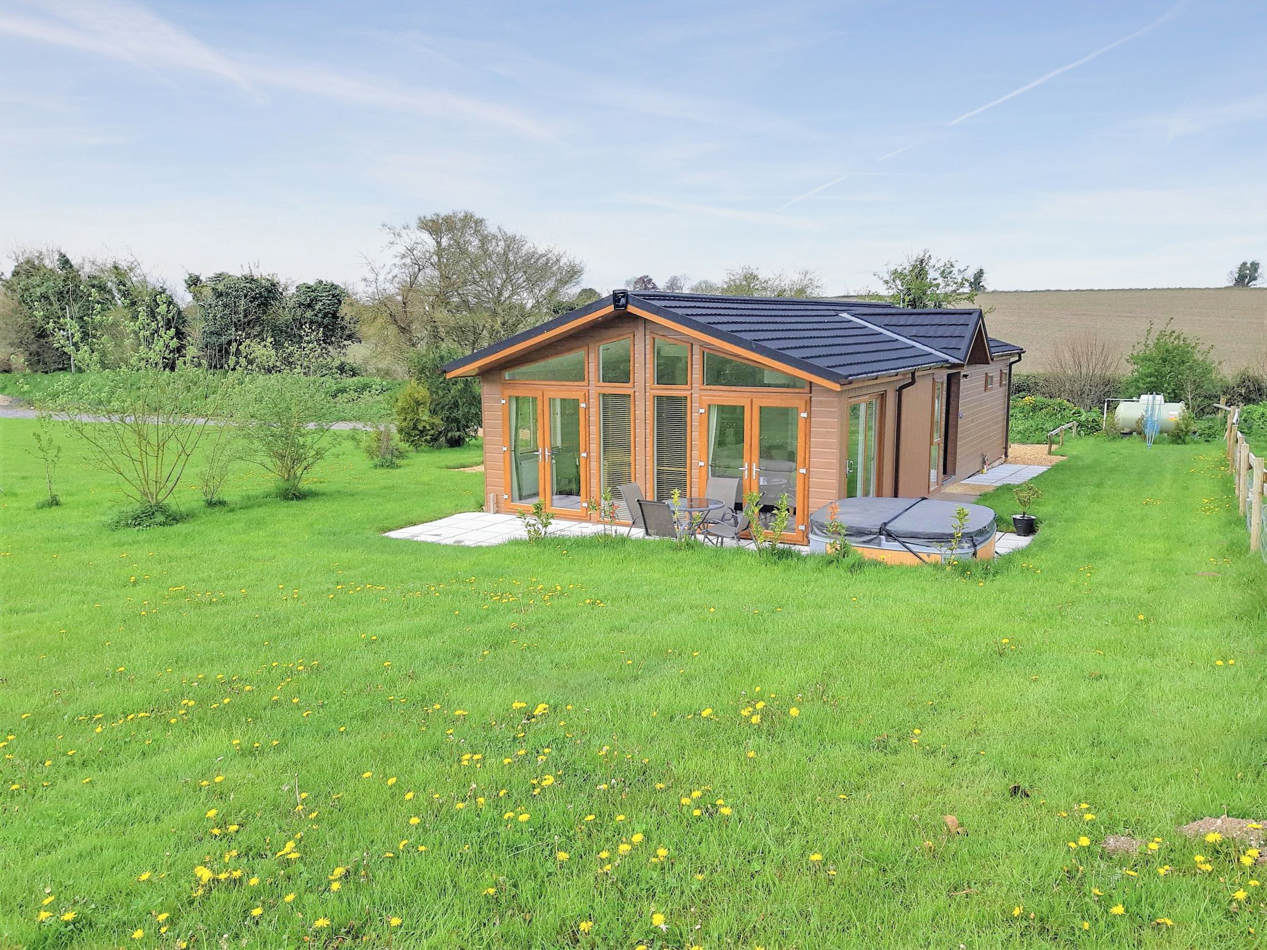 A modern house with a glass conservatory, a patio with outdoor furniture, and a well-maintained lawn.