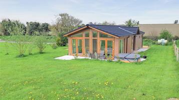 A modern house with a glass conservatory, a patio with outdoor furniture, and a well-maintained lawn.