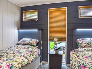 A bedroom with two beds, a nightstand, and a window with blinds.
