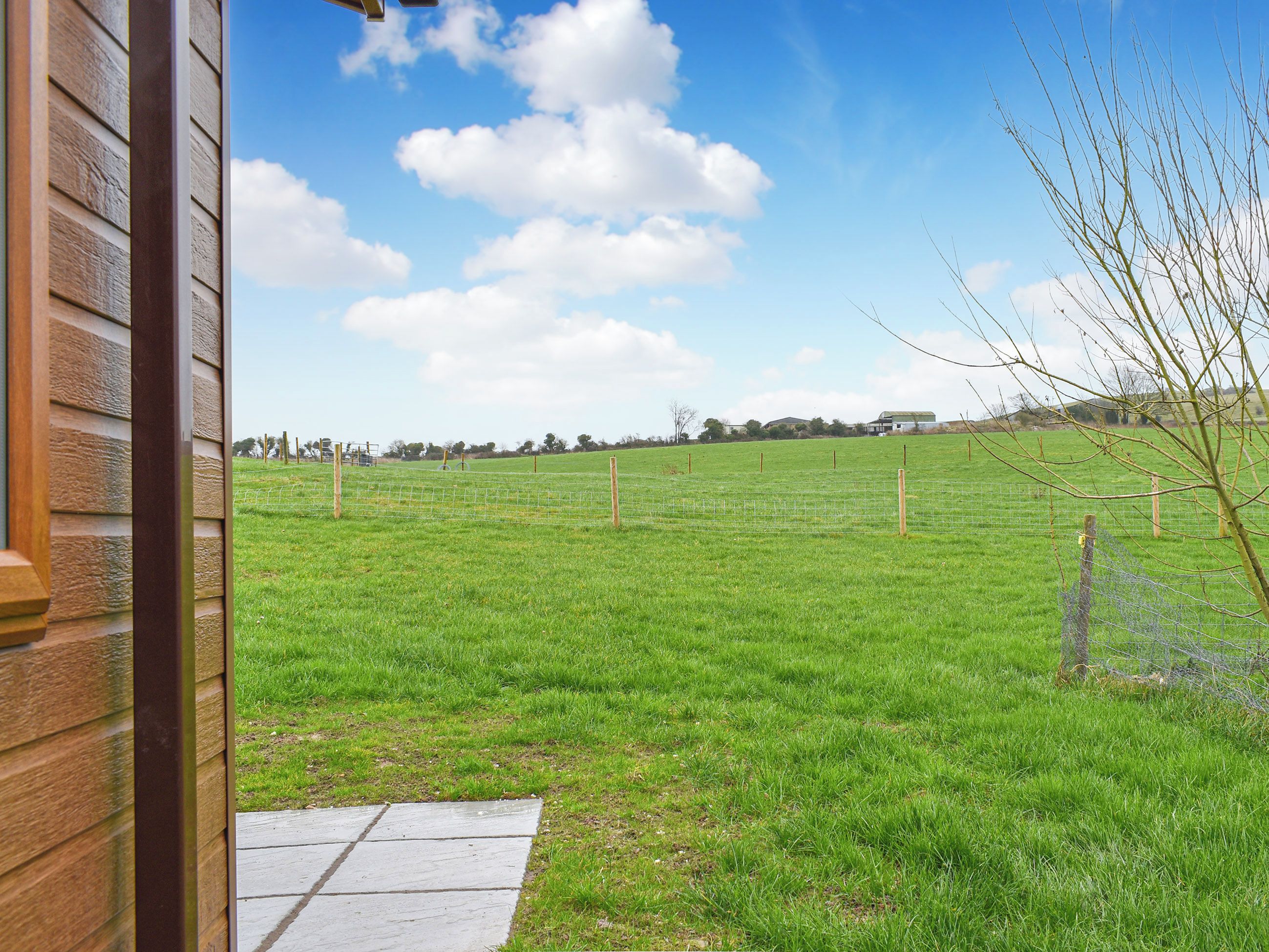 Ein grünes Feld mit einem Holzzaun, einem klaren Himmel und einem Gebäude im Hintergrund.