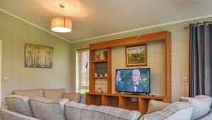 A living room with a grey sofa, a television on a wooden stand, and a painting on the wall. - Whitey Top Country Lodge (Pentridge)