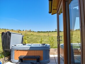 A hot tub on a patio with a view of a grassy field and a wooden fence.