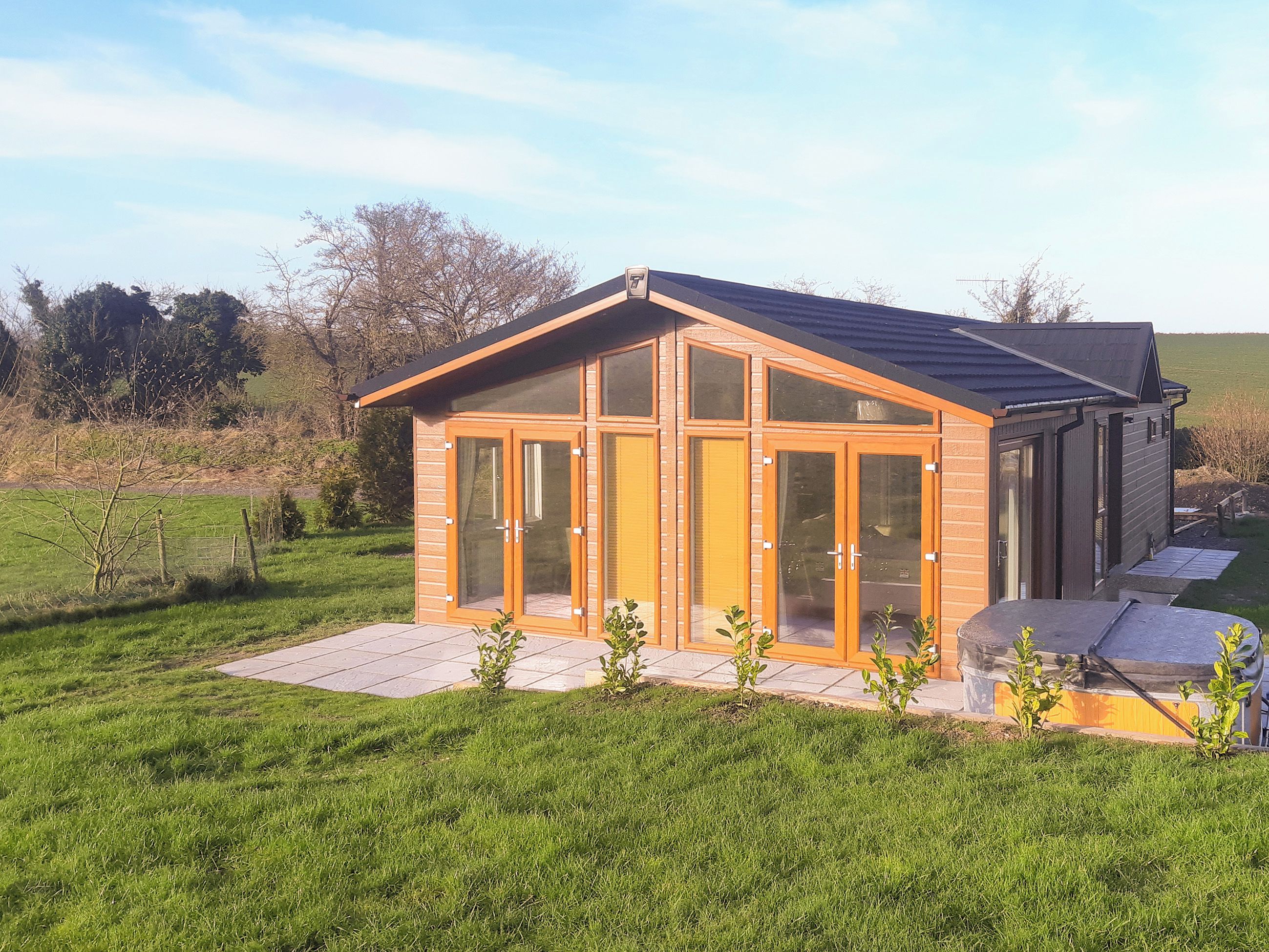A modern house with a large glass door, a tiled patio, and a grassy yard.