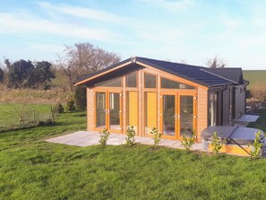 A modern house with a large glass door, a tiled patio, and a grassy yard.