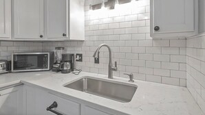 A modern kitchen with white cabinets, a stainless steel sink, a microwave, a coffee maker, and a blender. - LowerFlat in GermanVillage - 3BR Pet | Yard | Park (Columbus)