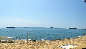 Une plage dallée de pierres, avec une échelle métallique qui descend dans l’eau, plusieurs bateaux et des îles au loin.