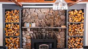 Un salon chaleureux avec une cheminée en pierre, des étagères à livres et une pile de bois de chauffage bien rangée.
