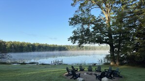 Un cadre idyllique au bord du lac, avec un quai, une balançoire et un espace aménagé avec un foyer et des fauteuils Adirondack.