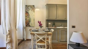 A dining area with a wooden table set for two, a painting on the wall, and a kitchen in the background. - Pontevecchio Stylish Apartment in Florence (Florence)