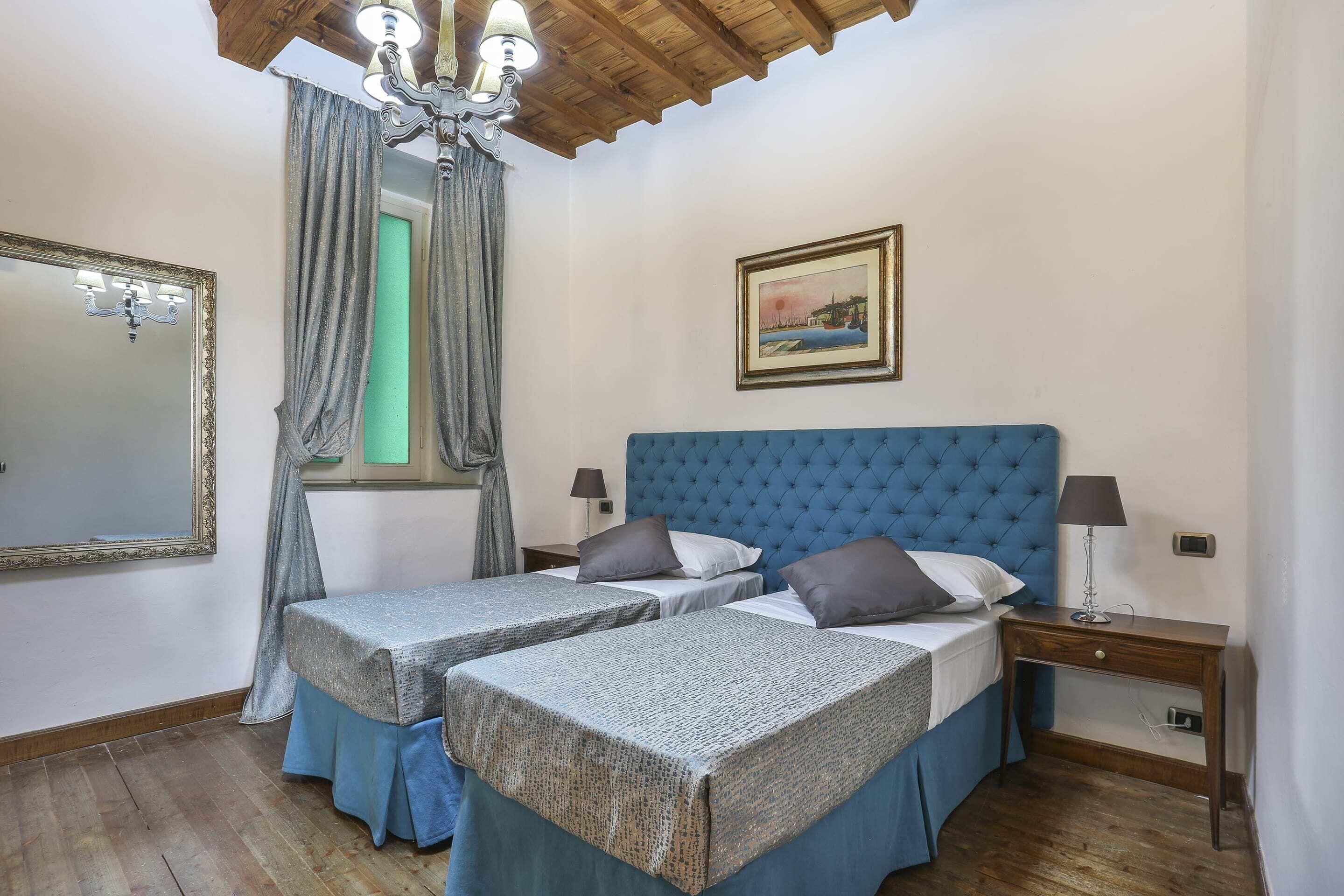 Quarto com duas camas de solteiro, um espelho grande, um candelabro, uma mesinha de cabeceira com luminária e um quadro na parede.