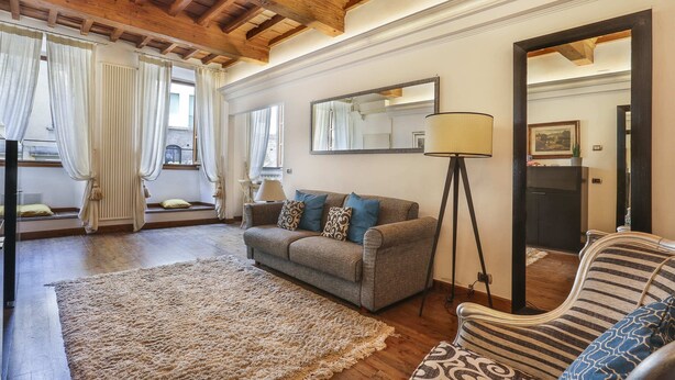 A living room with a sofa, a patterned armchair, a large rug, a floor lamp, and a mirror on the wall. - Pontevecchio Stylish Apartment in Florence (Florence)