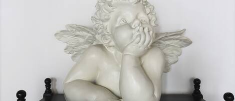 A white sculpture of a cherub with wings on a black table against a plain wall.