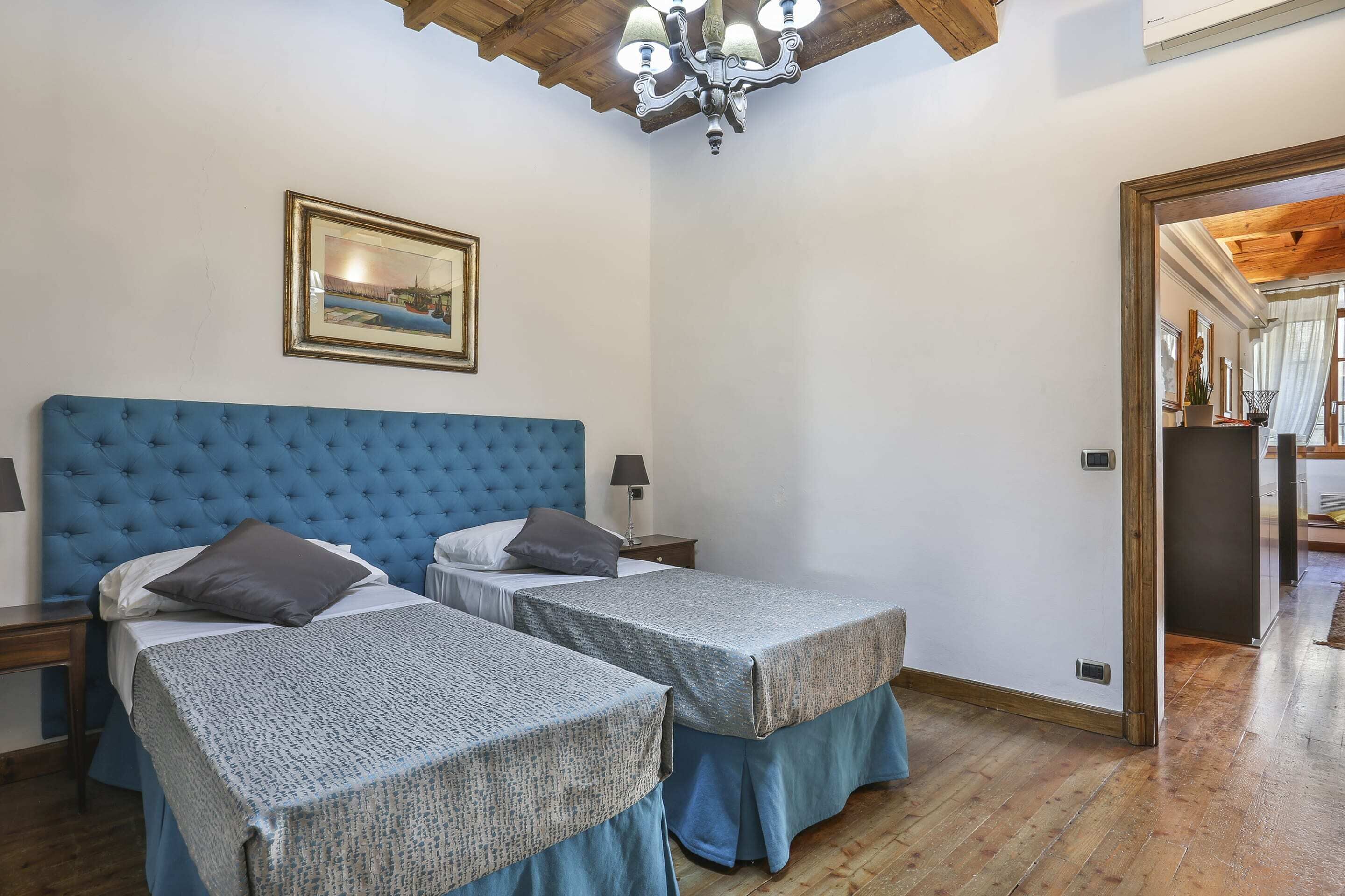Een slaapkamer met twee bedden, een kroonluchter, een ingelijst schilderij en een houten plafond.