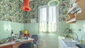 A kitchen with a tiled backsplash, a window with curtains, a sink, and a dining area with chairs and a table. - Lullaby Suite (Florence)