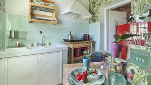 A kitchen with a white countertop, a sink, a wooden shelf with dishes, a red appliance, and a table with decorative items. - Lullaby Suite (Florence)