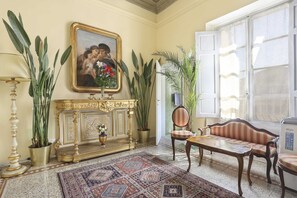 A room with a patterned rug, a sofa, a table, a fireplace, and large potted plants. - Lullaby Suite (Florence)