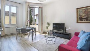 Un salon moderne avec un canapé rouge, une table à manger avec des chaises, un téléviseur et un tableau accroché au mur.