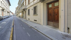 Une rue bordée de voitures garées et un immeuble doté d’une double porte et d’une fenêtre avec des barreaux.