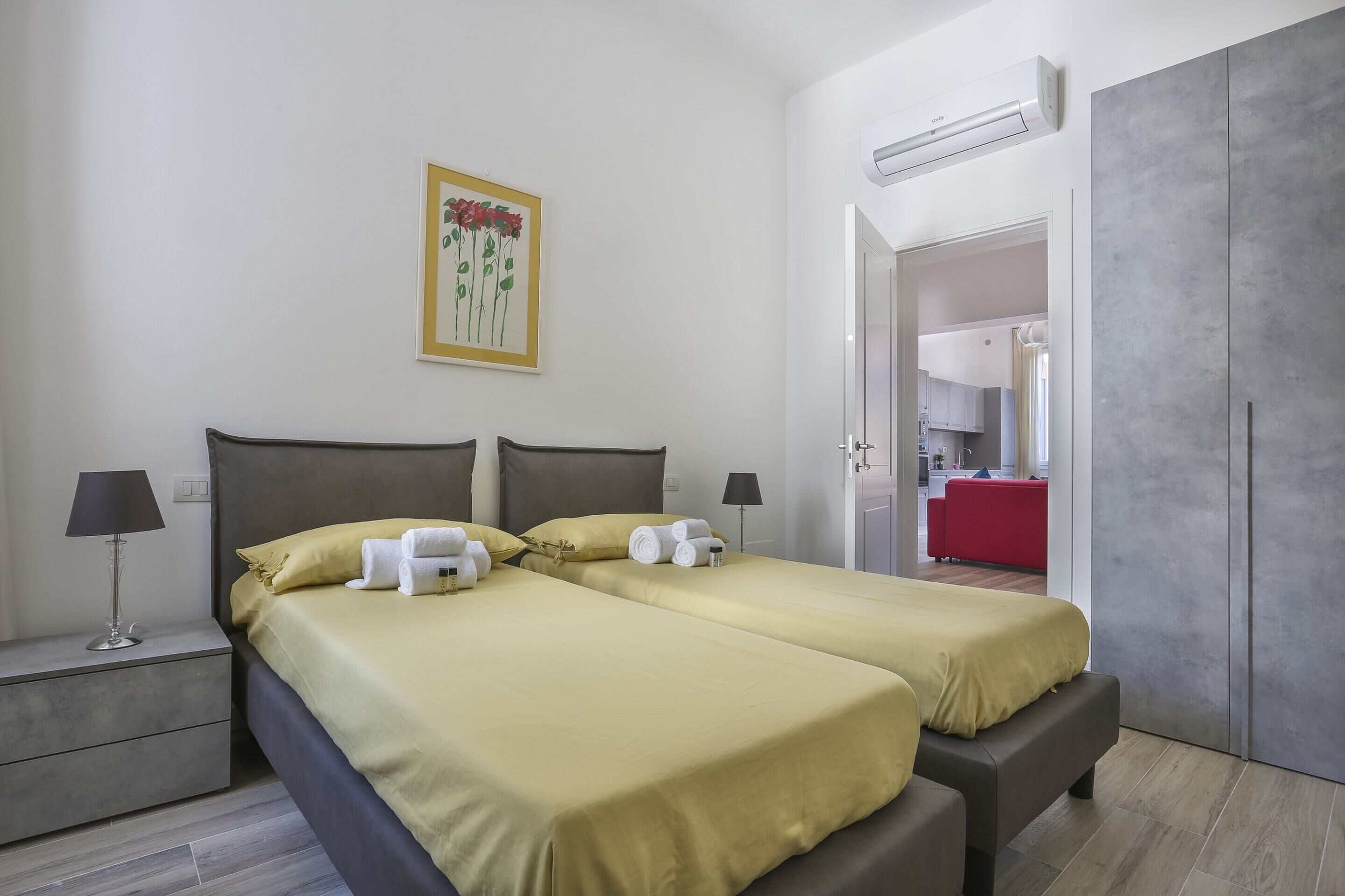Un lit double avec une literie jaune, une table de chevet avec une lampe et un tableau de fleurs accroché au mur.