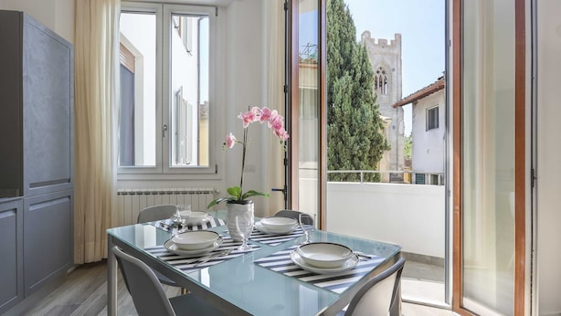 Un coin repas avec une table dressée pour quatre personnes, une orchidée en pot et une vue sur un château par la fenêtre.