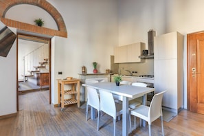 A modern kitchen with white cabinetry, a dining table with chairs, and a wooden staircase leading to an upper level. - Uffizi Suite II (Florence)