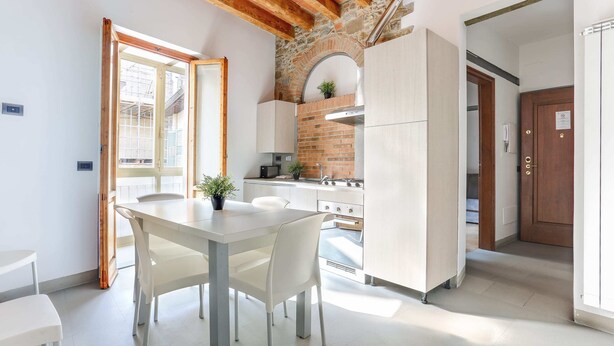 Una cocina moderna con armarios blancos, una pared de ladrillo y una zona de comedor con mesa y sillas.