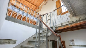 Una escalera con barandilla de madera y balaustres de metal, que conduce a un segundo piso con techo inclinado y vigas de madera.