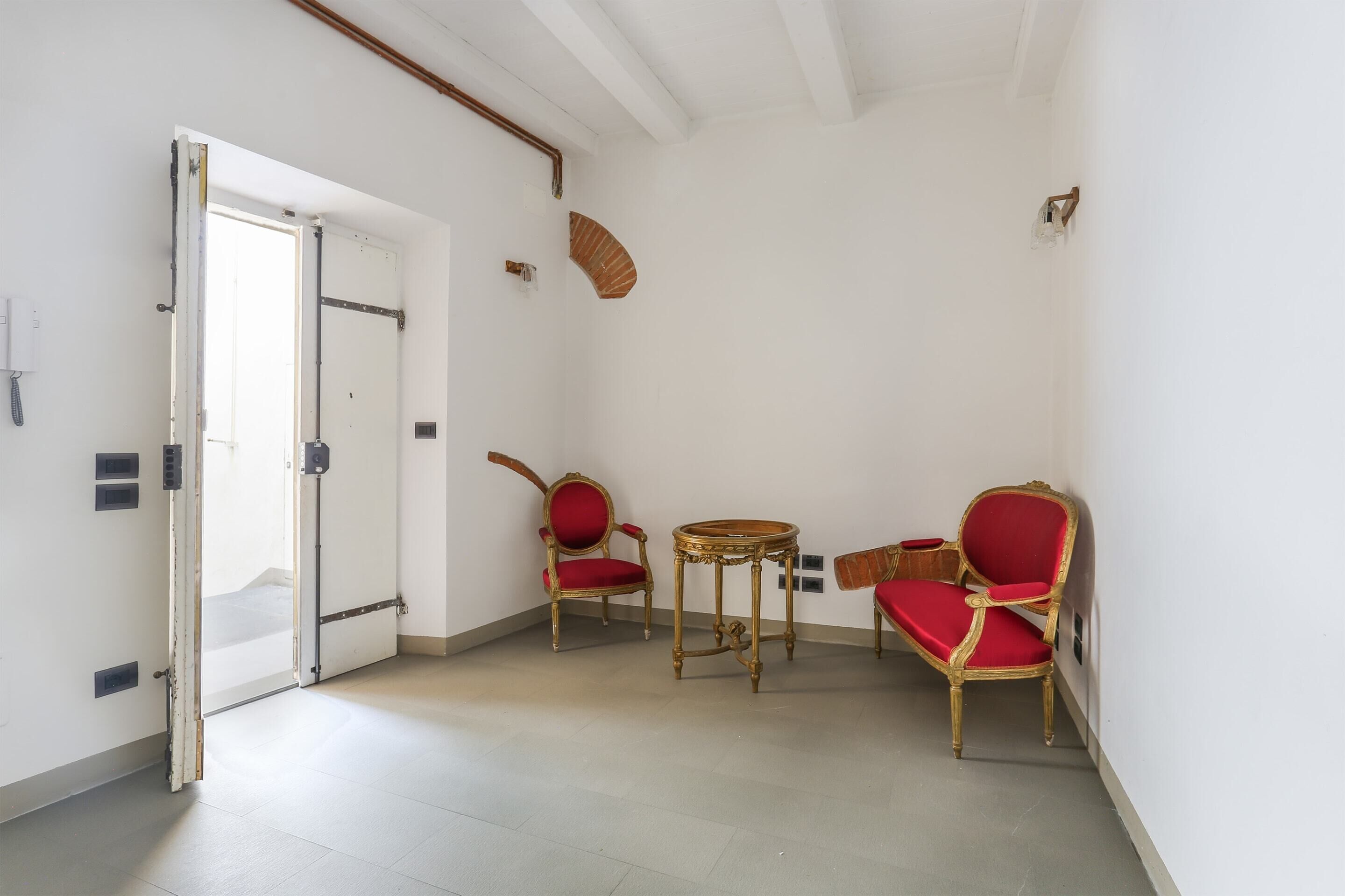 A room with a white door, a small round table, and two red upholstered chairs.