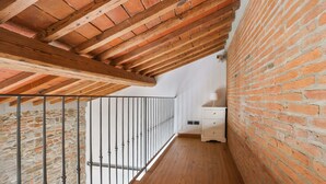 Un pasillo estrecho con suelo de madera, paredes de ladrillo y baranda metálica.