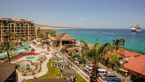 A resort with multiple swimming pools, a beach, and a cruise ship in the background.
