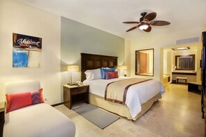 Ein Hotelzimmer mit einem Bett, zwei Nachttischen, einem Deckenventilator, einem Schminktisch und Bildern an den Wänden.