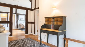 Um quarto com piso de madeira, um tapete estampado, um armário de madeira escura com uma luminária e uma porta branca que dá para outro cômodo.