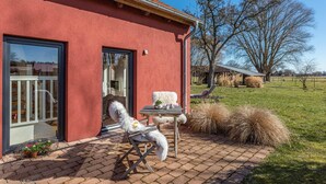 A red building with a brick patio, a white chair, and a table with a plant. - Manor Bockelkathen – Apartment 7 (Lüdersburg)