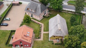 An aerial view of a residential area with two houses, one with a red roof and another with a grey roof, surrounded by greenery and a paved driveway. - Manor Bockelkathen – Apartment 7 (Lüdersburg)