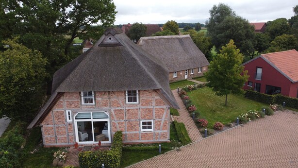 A traditional half-timbered house with a steeply pitched thatched roof, a large front door, and a visible chimney. - Manor Bockelkathen – Apartment 7 (Lüdersburg)