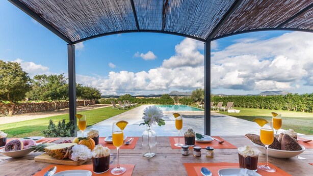 A table set for a meal with a view of a pool and mountains. - Modern villa in Mallorca Pleta with swimming pool (Manacor)