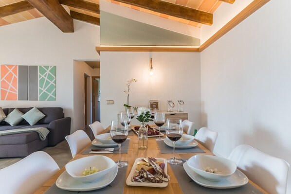 A dining area with a wooden table set for six, surrounded by white chairs. There are plates with food and wine glasses on the table. - Modern villa in Mallorca Pleta with swimming pool (Manacor)