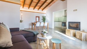 A modern living room with a sofa, a dining table with chairs, a small round table with a plant, and a kitchen area with a stove and oven. - Modern villa in Mallorca Pleta with swimming pool (Manacor)