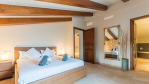 A bedroom with a wooden bed, white linens, a nightstand with a lamp, and a large mirror. - Modern villa in Mallorca Pleta with swimming pool (Manacor)