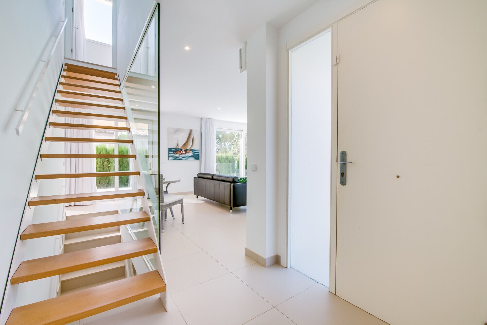 A modern interior with a wooden staircase, a dining area, and a door leading to another room.