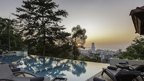 Ein Infinity-Pool mit Liegestühlen und Blick auf die Stadt bei Sonnenuntergang.