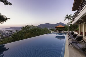 Ein Pool mit Überlauf auf dem Dach, mit Liegestühlen, einer Laube und Blick auf Stadt und Berge.