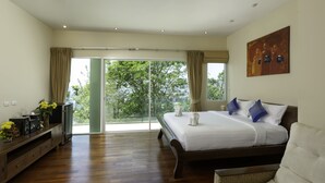 Ein Schlafzimmer mit einem großen Bett, einem Fernseher und Blick auf Bäume durch die Glasdoor.
