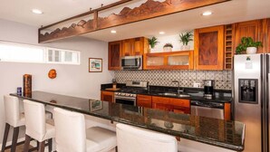 A modern kitchen with wooden cabinets, a granite countertop, and bar stools. - Casa Azul (Seal Beach)