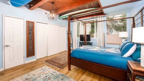 A bedroom with a four-poster bed, wooden ceiling beams, and a large window with a view of the outdoors. - Casa Azul (Seal Beach)