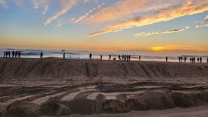 A beach with people walking along the shore, a sunset in the background, and a sandy area with tire tracks. - Casa Azul (Seal Beach)
