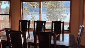 A dining area with a wooden table and chairs, large windows with a view of trees and a body of water. - Large 3-story LAKE VIEW 4 bedrooms (all masters) & 5 bath Boat Slip & Marina (Bass Lake)